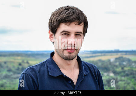 Portrait of serious casual young man standing against natural background Stock Photo