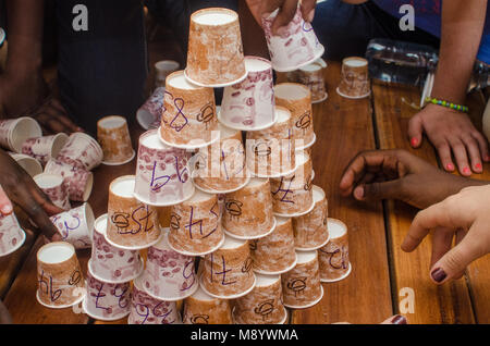 A paper cup tower with numbered cups sits on a table while small hands can be seen adding to the tower. Kids work on a project at international school. Stock Photo