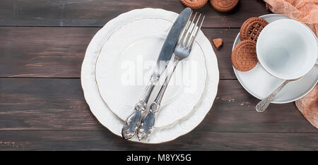 Empty white plates with silverware  knife and fork , cup ,jug and chocolate cookies  on dark wooden table background. Table setting. plate fork knife  Stock Photo