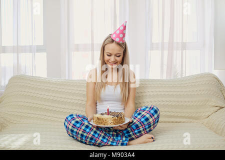 A blonde girl in a pajama cap with a cake with a candle celebrat Stock Photo