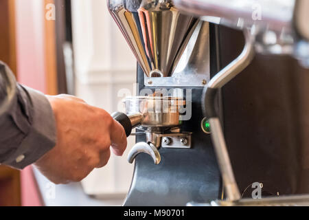 Barista holding portafilter in hand and grinding coffee beans with grinder to making espresso or cappuccino Stock Photo