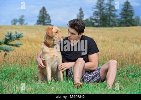 young man with his yellow lab sitting in the field Stock Photo