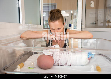 Woman looking on her baby in hospital cradle Stock Photo