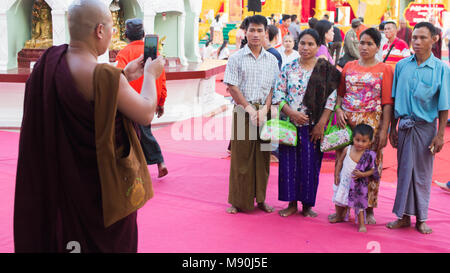 Yangon, Myanmar - February, 15, 2018: a Burmese monk taking picture for a group of Buddhist worshipers at Shwedagong Pagoda