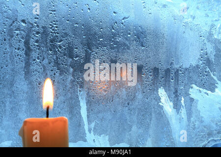 Candle with burning flame on background with frozen wet window Stock Photo