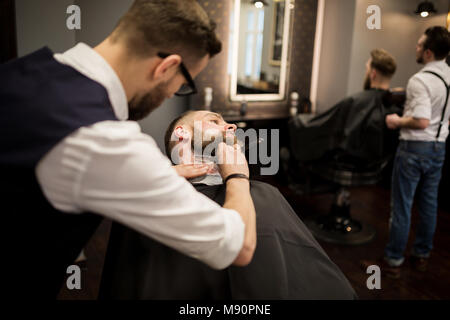 Portrait of barber shaving young man with razor Stock Photo