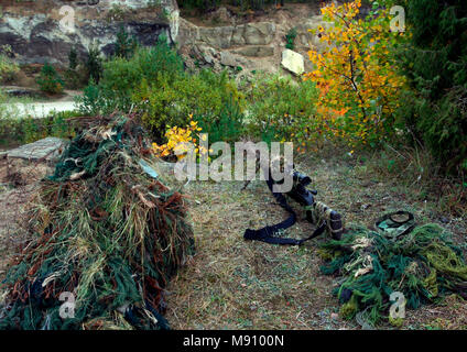 Camouflage Hunter or soldier hiding in bushes in camouflage autumn  background. Sniper with rifle. Stock Photo