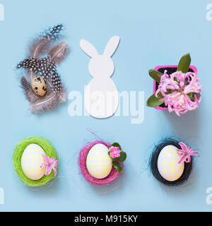 Easter concept. White bunny and painted chicken eggs with pink flower decor on blue. Top view. Flat lay. Stock Photo