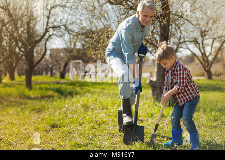 Pleasant aged man digging with his grandson in the garden Stock Photo
