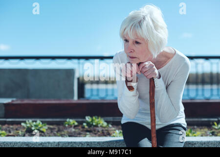 Washed up senior woman leaning on cane and dreaming Stock Photo