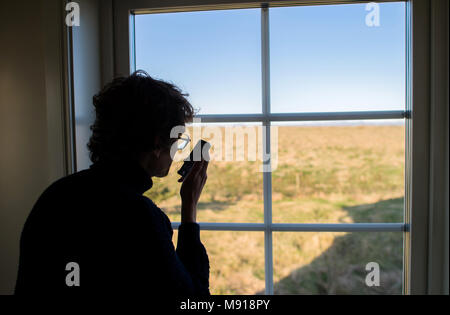 Man using a cell phone near a window. Iceland. Stock Photo