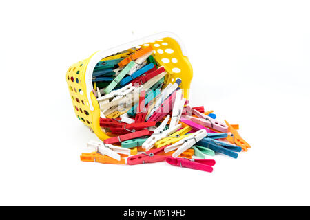 Pile of colourful plastic cloth clamps inside yellow basket isolated on white background. Stock Photo
