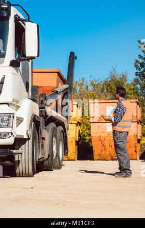 Worker on construction site unloading container for waste from truck Stock Photo