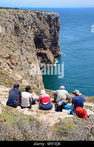 Five tourists sitting in a row enjoying the views, Cape St Vincent, Algarve, Portugal, Europe. Stock Photo