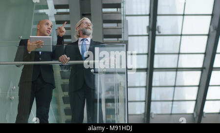two design professionals standing in modern glass and steel building having a discussion using digital tablet. Stock Photo