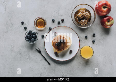 top view of sweet homemade pancakes with fresh berries and honey on grey