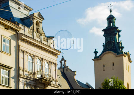 Big soap bubble flies through air in city. Flying soap bubble with reflection against blue sky Stock Photo