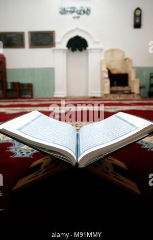 An open Holy Quran on wood stand with mihrab in background. Stock Photo