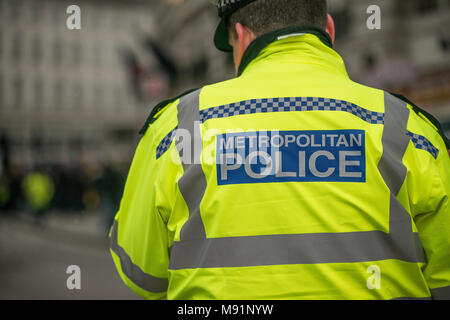 Police officer with his back to camera with Metropolitan Police sign on his yellow reflective jacket.. Stock Photo