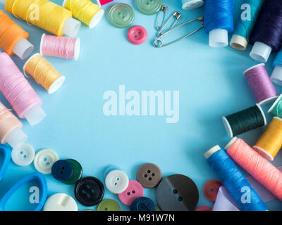 Multicolored sewing threads and buttons on blue background with copy space flat lay. Stock Photo
