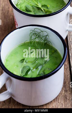 Cream soup with green pea, fresh herbs and sprouts with micro greens on top in rural mugs, healthy vegetarian meal Stock Photo