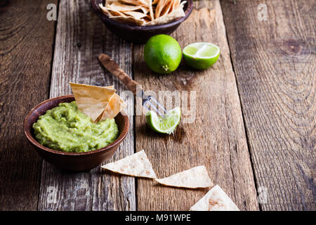 Fresh guacamole dip with lime juice served with handmade nachos on wooden rustic table, traditional Mexican style avocado sauce in ceramic bowl, healt Stock Photo