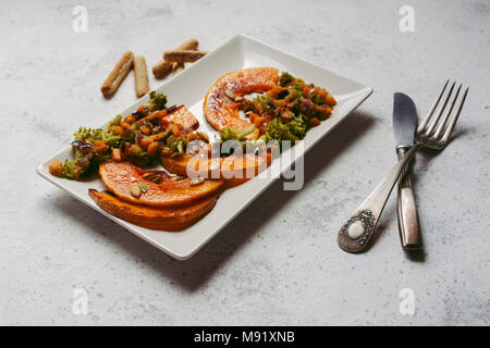 sliced baked pumpkin, with broccoli and assorted vegetables, on rectangular white plate Stock Photo