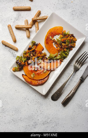 sliced baked pumpkin, with broccoli and assorted vegetables, on rectangular white plate, from above Stock Photo