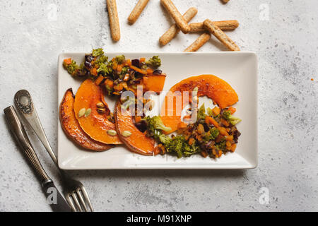 sliced baked pumpkin, with broccoli and assorted vegetables, on rectangular white plate Stock Photo