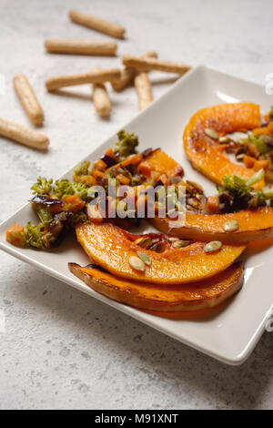 sliced baked pumpkin, with broccoli and assorted vegetables, on rectangular white plate Stock Photo