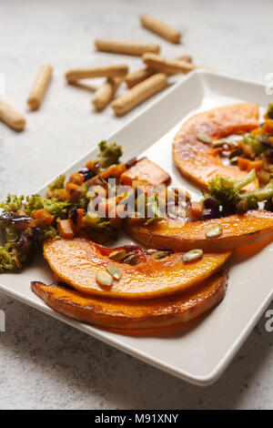 sliced baked pumpkin, with broccoli and assorted vegetables, on rectangular white plate Stock Photo