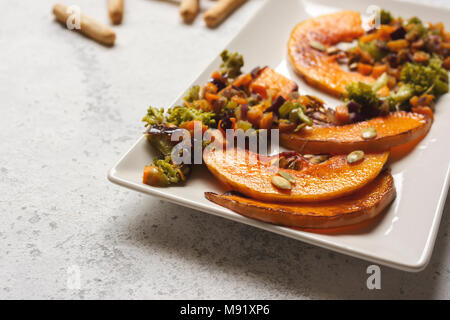 sliced baked pumpkin, with broccoli and assorted vegetables, on rectangular white plate Stock Photo