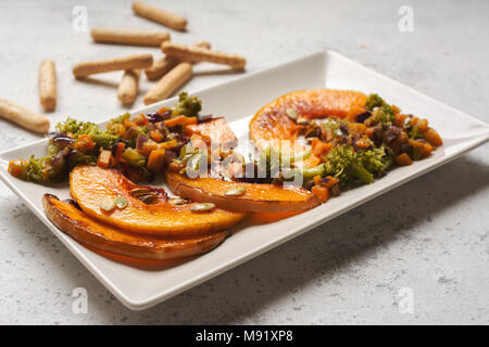 sliced baked pumpkin, with broccoli and assorted vegetables, on rectangular white plate Stock Photo