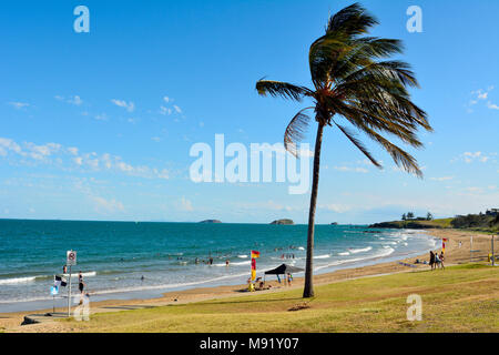 Emu Park, Queensland, Australia - December 27, 2017. Beach in Emu Park, QLD, with people, palm tree and surf rescue flags. Stock Photo