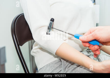 Neurological physical examination of the elbow flexion reflex. Doctor neurologist with a neurological hammer in his hand checks the status of the patient's reflexes in office in hospital. Stock Photo