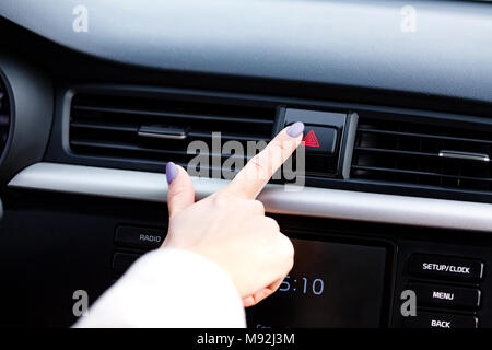 Closeup shot of woman's manicured finger pressing the emergency button on a car's dashboard Stock Photo