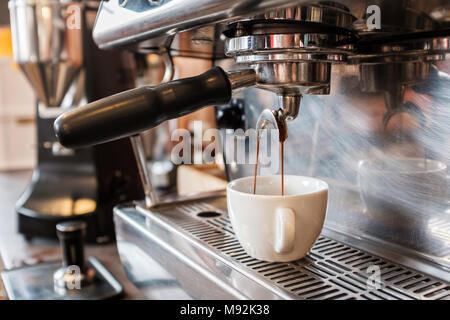 Fresh espresso dripping from portafilter of coffee machine into white cup Stock Photo