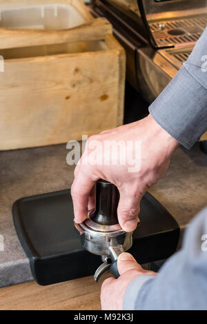 Barista pressing freshly ground coffee with tamper in portafilter to making espresso or cappuccino Stock Photo