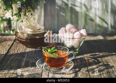 Delicious strawberry green mint tea in a transparent glass teapot and Cup in the summer, on a rustic wooden table with marshmallows. Copy spase A hori Stock Photo