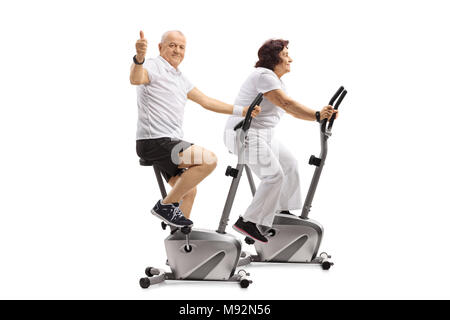 Mature man and a mature woman on exercise bikes with the man making a thumb up sign isolated on white background Stock Photo