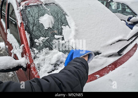 Driver cleaning snow from windshield of car using scraper. Stock Photo