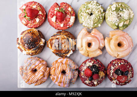 Variety of colorful old fashioned fried gourmet donuts on a marble surface with glaze Stock Photo