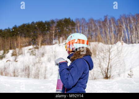 Photo of side view of sporty woman in helmet with snowboard looking at camera Stock Photo
