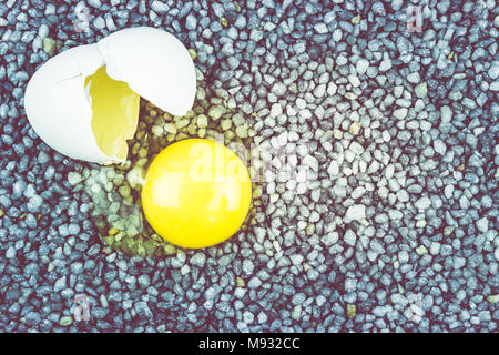 Broken egg on gray gravel, asphalt. The risk of loss, ruin. Stock Photo