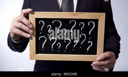 Question marks written on blackboard, male wearing classic suit holding a sign Stock Photo