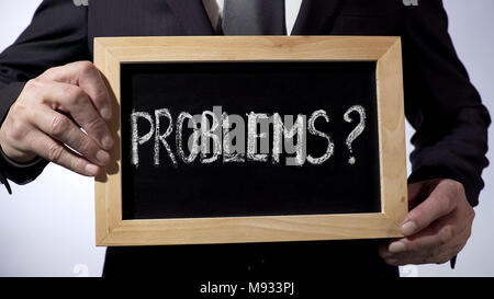 Problems with question mark written on blackboard, businessman holding sign Stock Photo