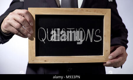 Questions written on blackboard, business person holding sign, FAQ, advice Stock Photo