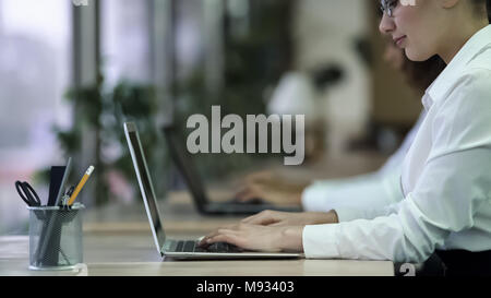 Successful female typing e-mail on laptop, smiling woman enjoying work at office Stock Photo