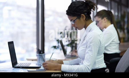 Mixed-race business woman making notes on paper, hard-working office manager Stock Photo