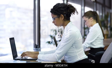 Pretty mixed-race lady typing on laptop, working for company support center Stock Photo